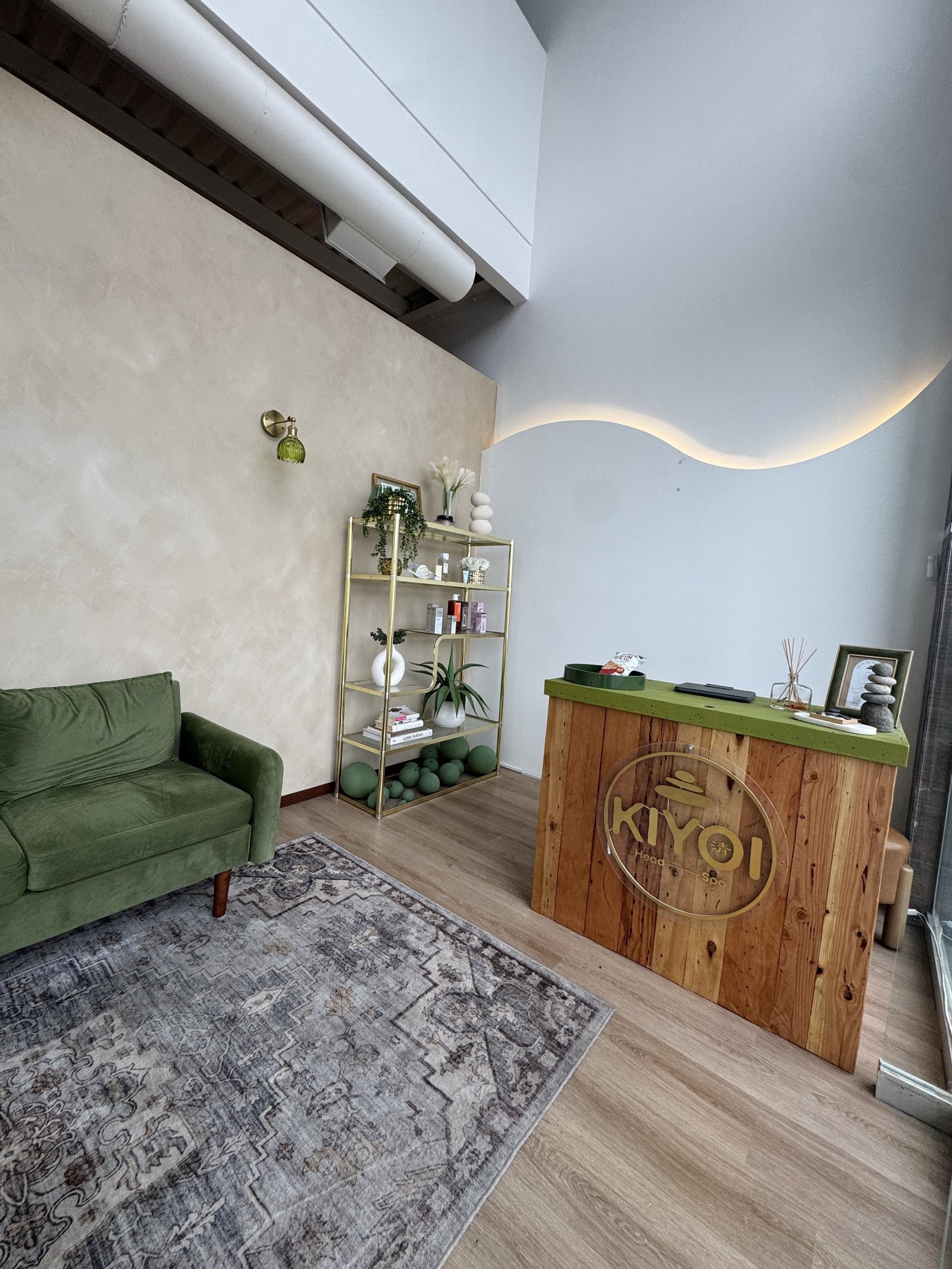 Sala de espera KIYOI con sofá verde, estantería dorada y escritorio de madera con logo